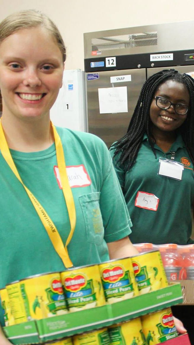 Two students holding containers of canned food and drinks.